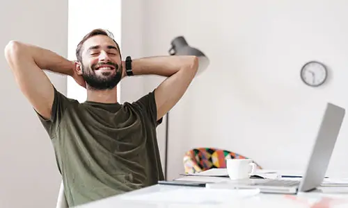 Man relaxing at desk with hands behind his head.
