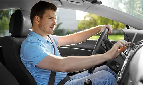 Man driving car with one hand on steering wheel and the other using cell phone screen.