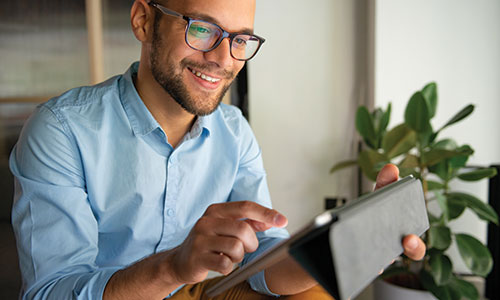 Young man using iPad while smiling and pointing at screen.