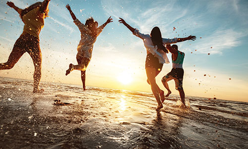 Four friends running through ocean at sunset