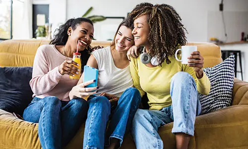 Three girlfriends relaxing together on couch to fit in view of phone screen.