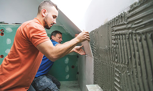 Two men installing tile on walls.