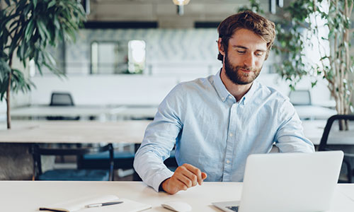 Man sitting in modern workspace at table working on laptop.