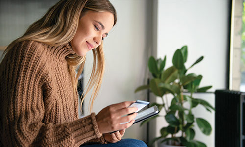 Young woman looking at credit card in hand while holding tablet in the other.