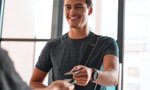 Young man with messenger bag across him handing merchant a form of payment.