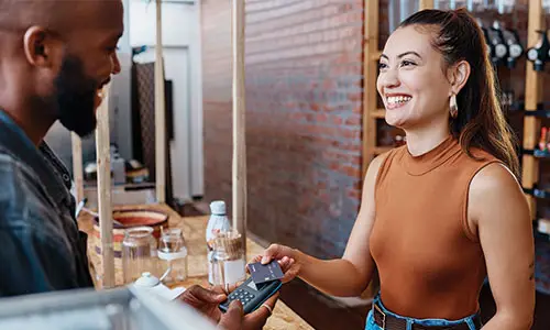 Happy woman handing male employee credit card in restaurant.