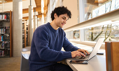 Young man in library using table to work on laptop.