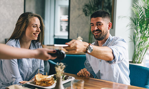 Man and woman eating in restaurant while using contactless pay to purchase meal.