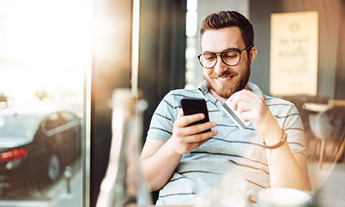 Man sitting comfortably in cafe paying on cell phone with credit card