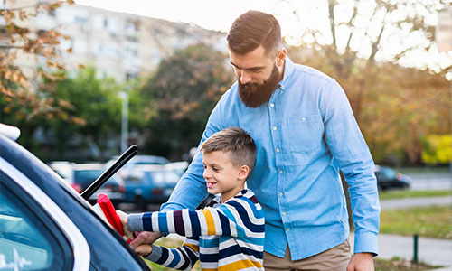 Father and son washing windows of car