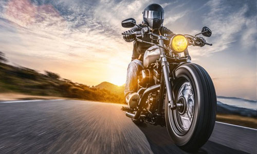 Motorcycler riding along road with full gear and helmet away from sunset.